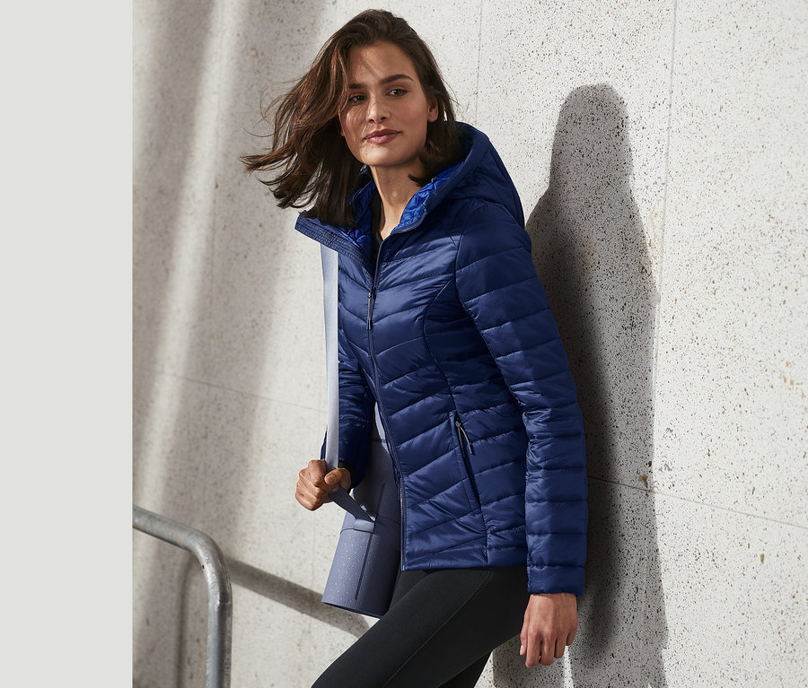 Nő sétál egy kék, könnyű steppelt kabátban.