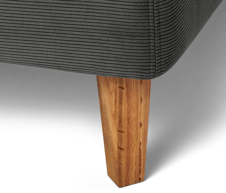 Egy antracit boxspring ágy részlete fa lábbal.