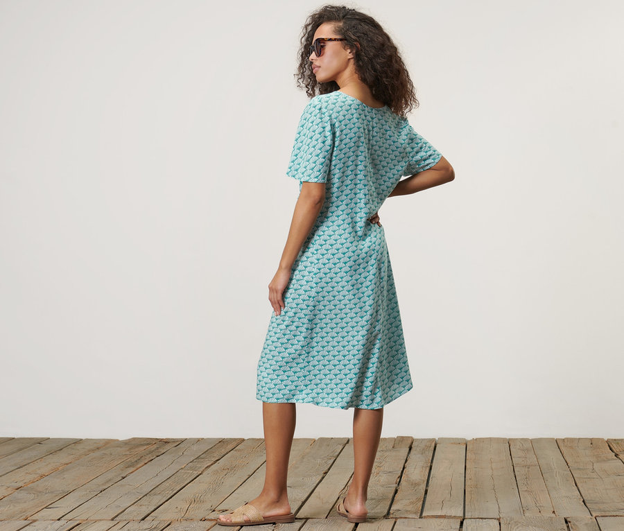 Nő kagyló mintás, türkiz ruhában pózol.