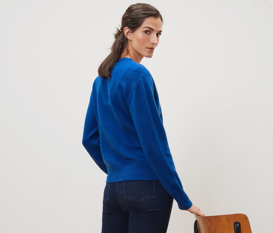 A nő a válla fölött hátra néz, kobaltkék, gyapjú kötött kardigánt visel.