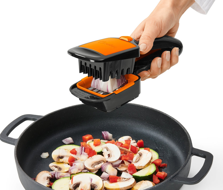 Egy kéz a Nicer Dicer Quick XXL aprítót használja hagyma felvágásához egy zöldségekkel teli serpenyő fölött.