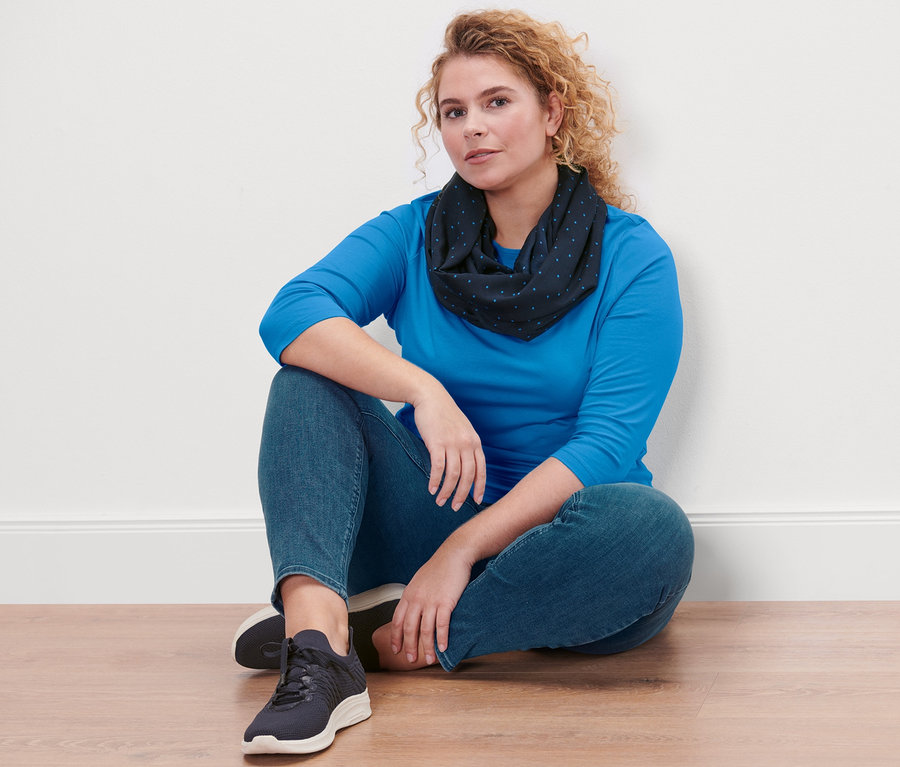 Egy nő ül a padlón, kék csónaknyakú felsőt, farmer hatású Fit Nelly treggingst és pöttyös csősálat visel.
