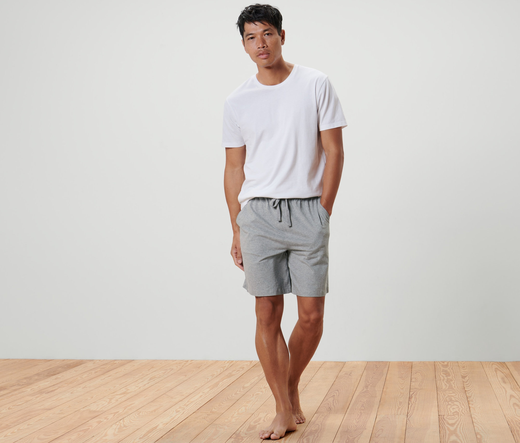 Egy férfi áll a Férfi jersey rövidnadrágban, melírozott szürke színben, kezével a zsebében.