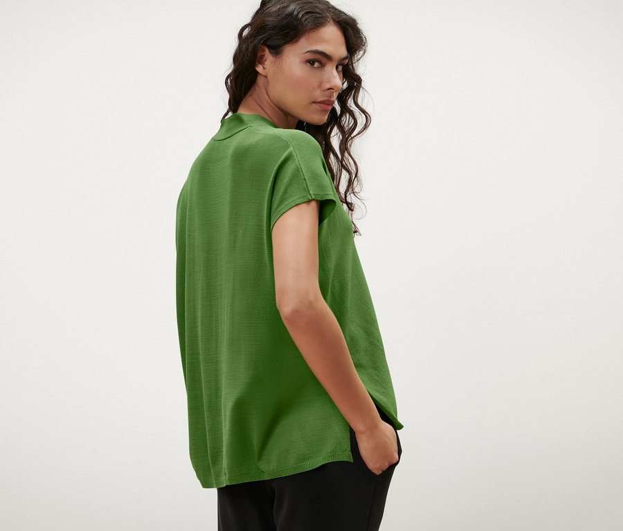 A nő a válla fölött hátra néz, és egy zöld, rövid ujjú kardigánt visel.