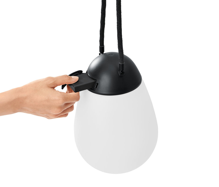 Egy kéz egy elemet helyez be egy LED-es akkus lámpába további pótakkumulátorral.