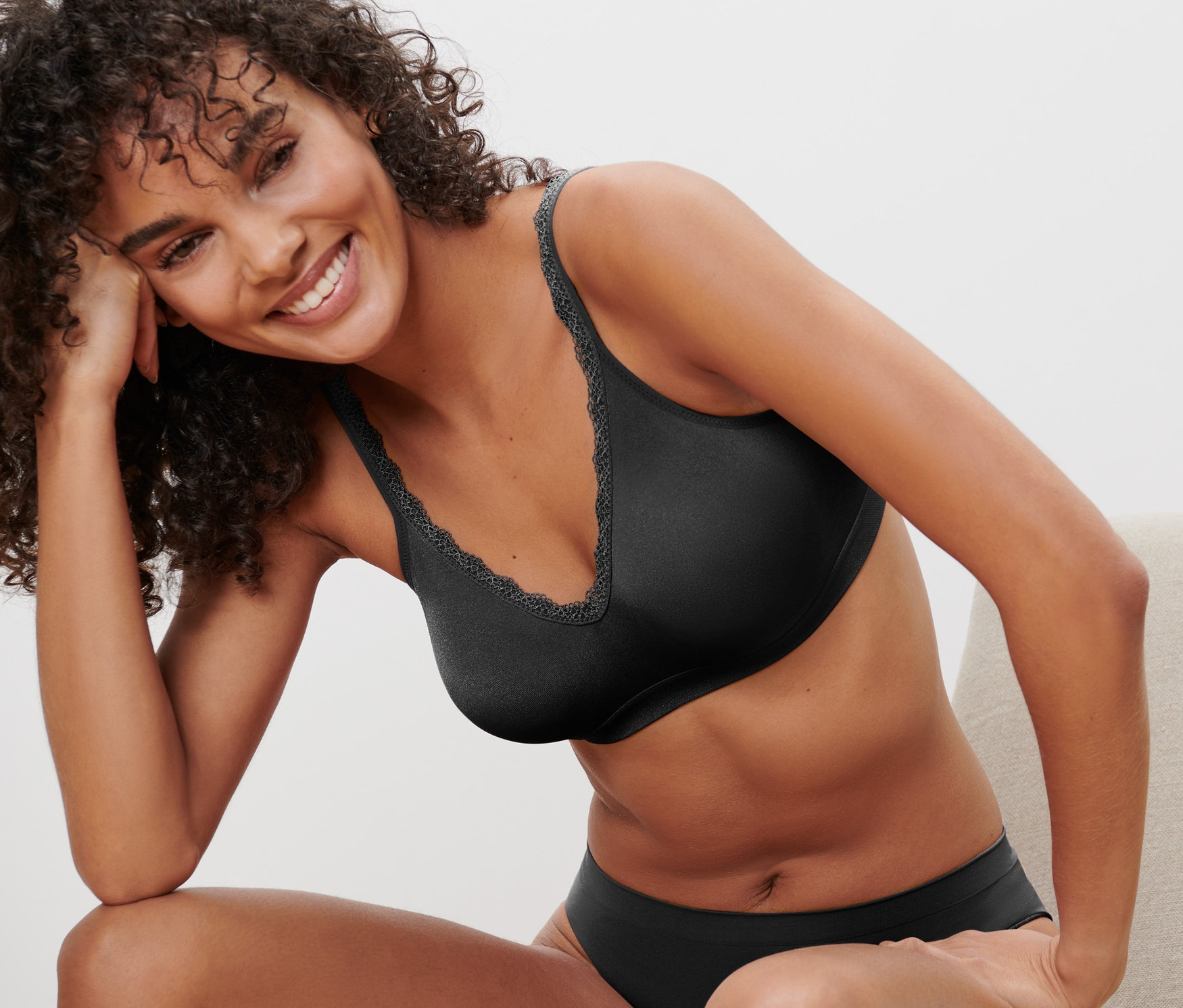 Mosolygó nő ül egy széken, fekete Seamless puha melltartót visel.