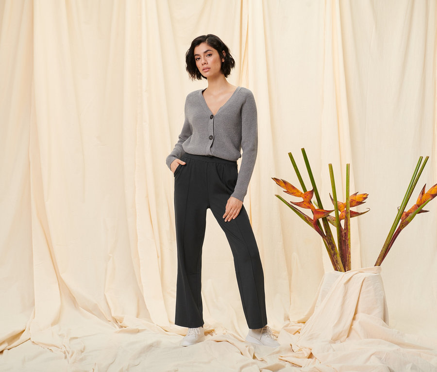 Nő pózol fekete női szabadidőnadrágban és szürke kötött kardigánban.