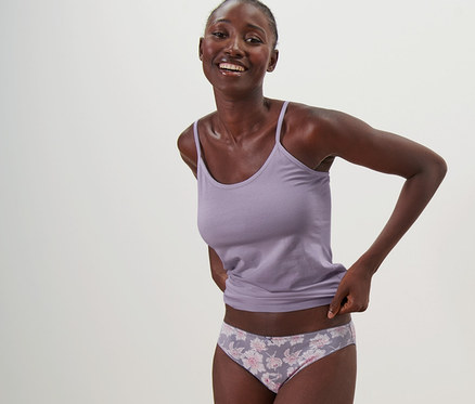 Mosolygó nő pózol trikóban és 5 db alsóban.