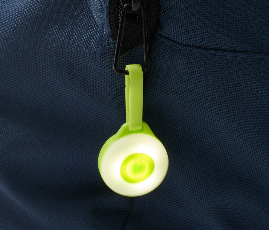 Egy zöld 3 LED-es lámpa, karabinerrel rögzítve egy kék táska cipzárjához.