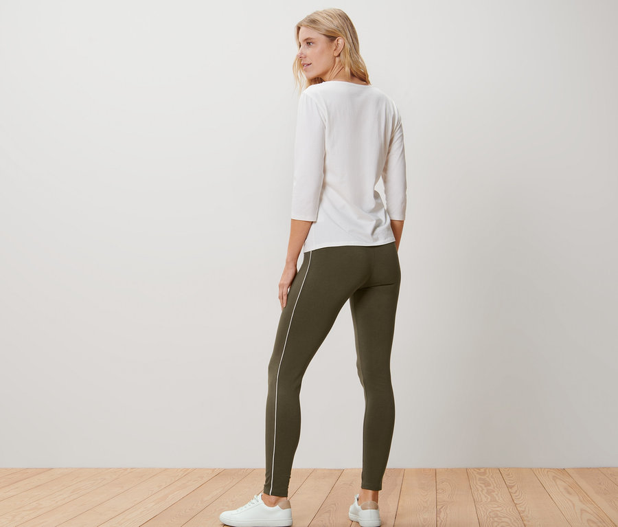 Hátulról látható nő fehér blúzt és olívazöld, paszpóllal ellátott leggingst visel.