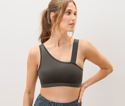 Nő pózol olívazöld bustier sportmelltartóban és levélmintás leggingsben.