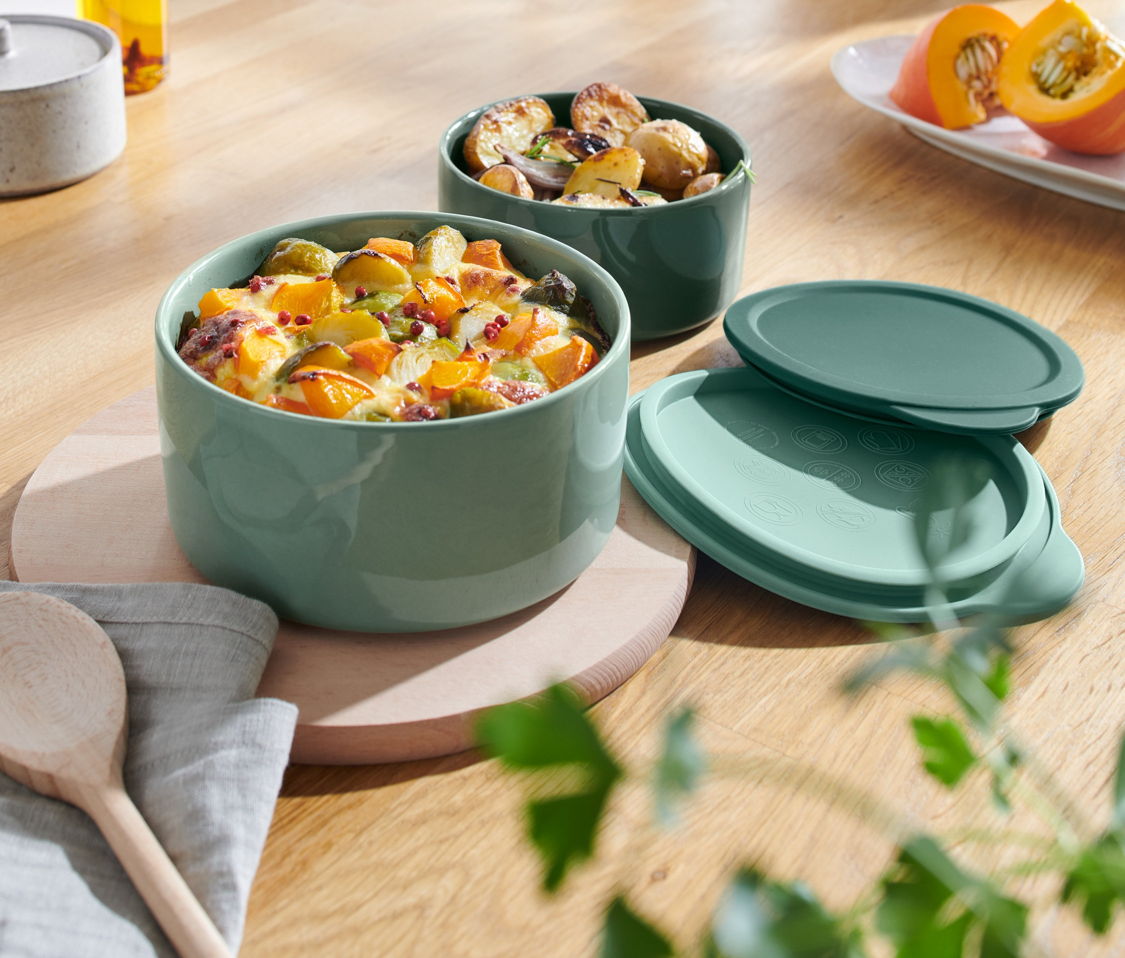 Két zöld kerámia sütőedény étellel egy fa asztalon.