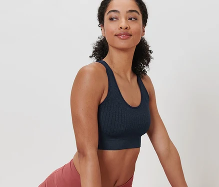 Nő sötétkék Seamless sportmelltartót és rózsaszín leggingset visel, és nyújtó gyakorlatokat végez egy szőnyegen.