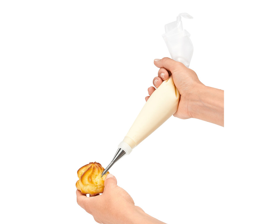 Egy kéz habcsókot tölt krémmel egy díszítőcső készlet segítségével.