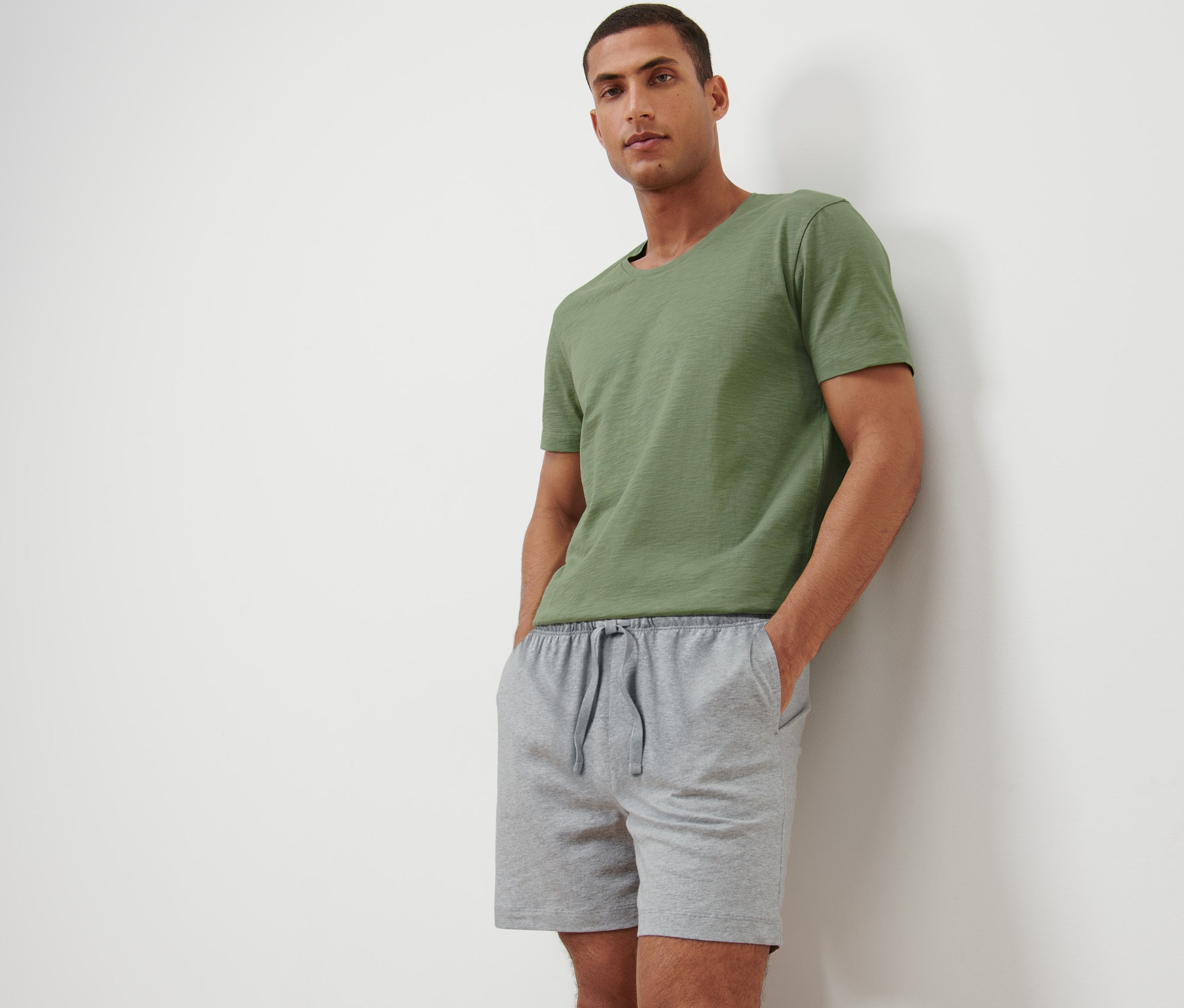 Egy férfi rövidnadrágos pizsamában és zöld pólóban pózol.