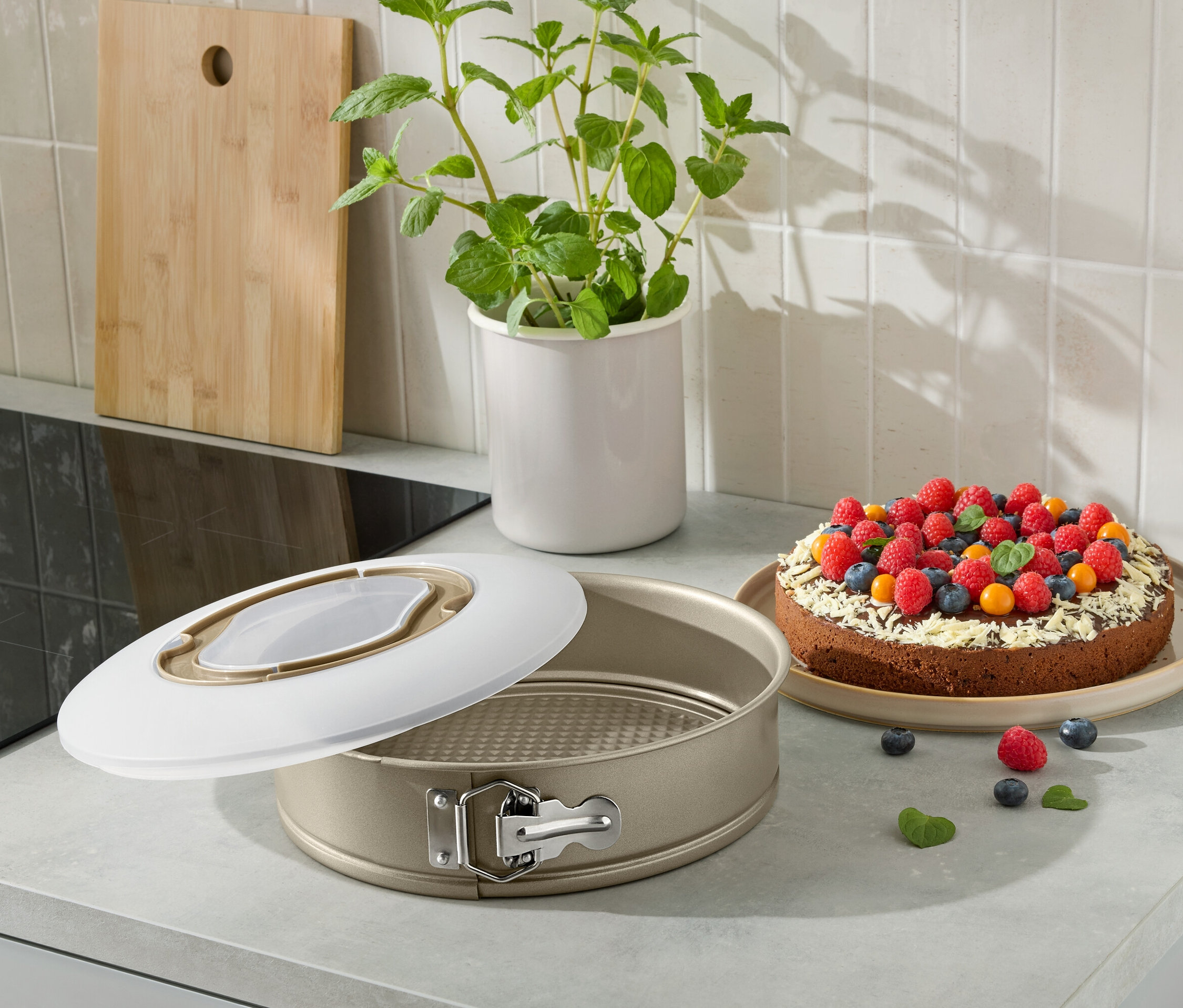 Egy nyitott tortaforma egy gyümölcsökkel díszített sült tortával a konyhapulton.