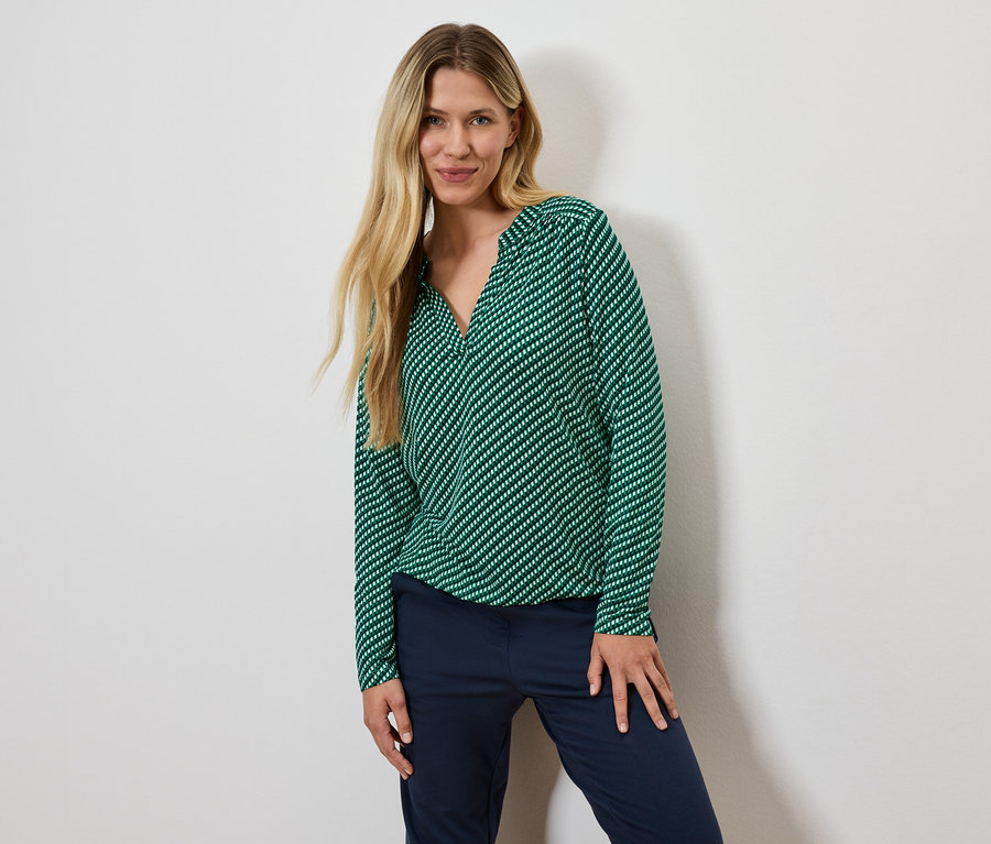Szöske nő zöld, csíkos blúzban és sötétkék nadrágban pózol.
