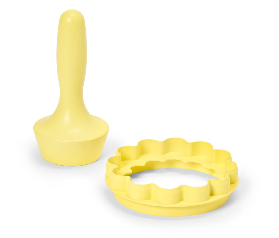 Sárga tészta nyomó fogantyúval és hullámos szélű kerek nyomó fehér háttérrel.