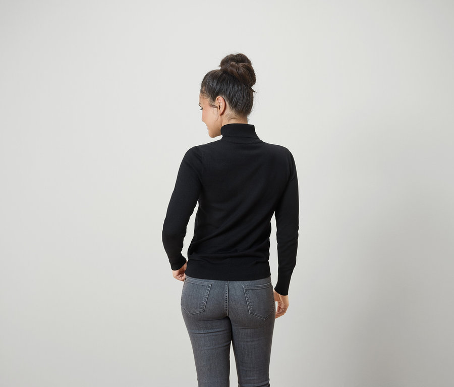 Hátulról látható egy kontyba fogott hajú nő, aki fekete garbót és szürke farmert visel.