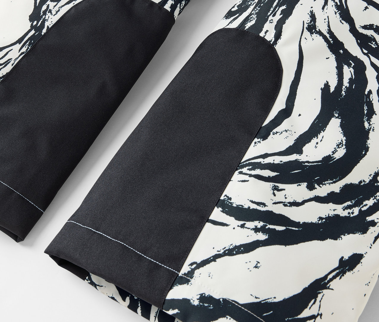 Egy fekete-fehér nadrág részlete absztrakt mintával és fekete térdfoltokkal.