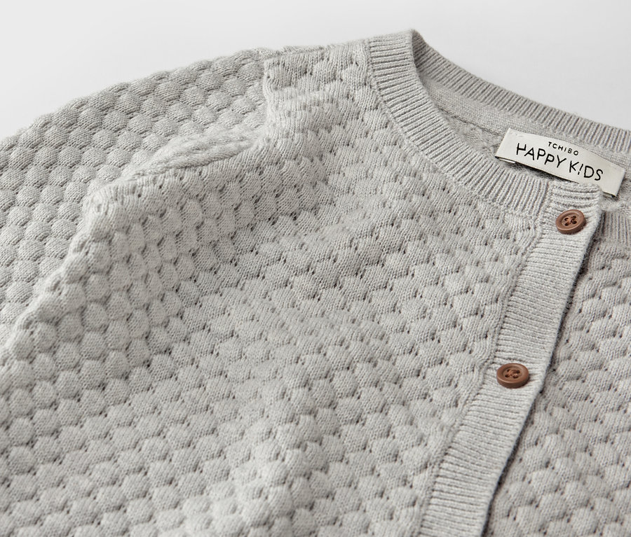 Egy szürke kötött kardigán részlete közelről.