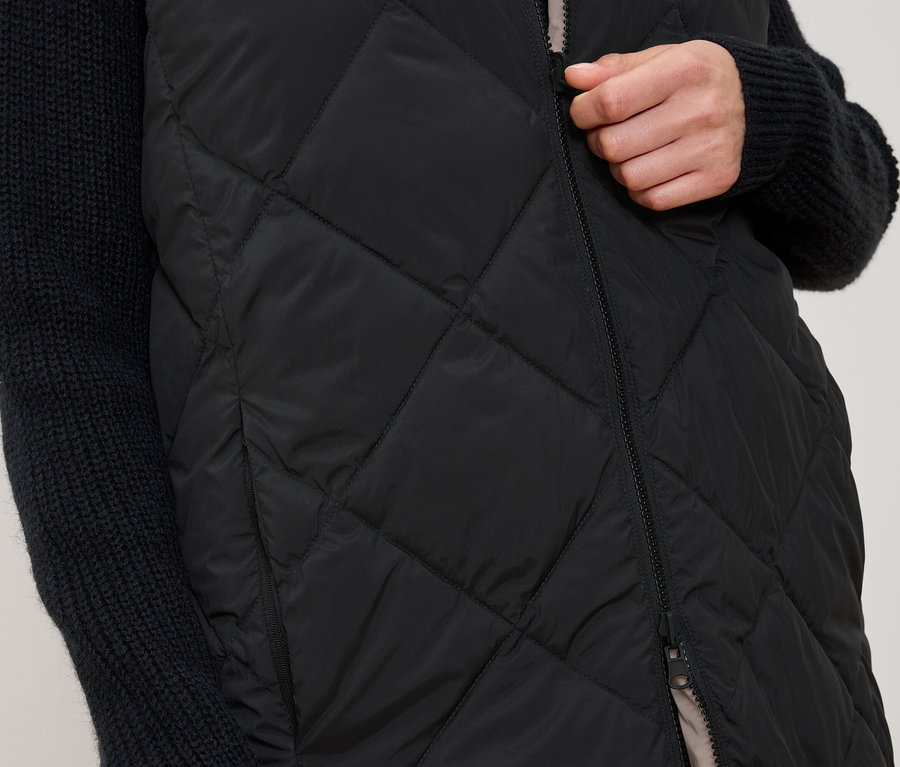 Nő cipzározza a fekete steppelt mellényt.