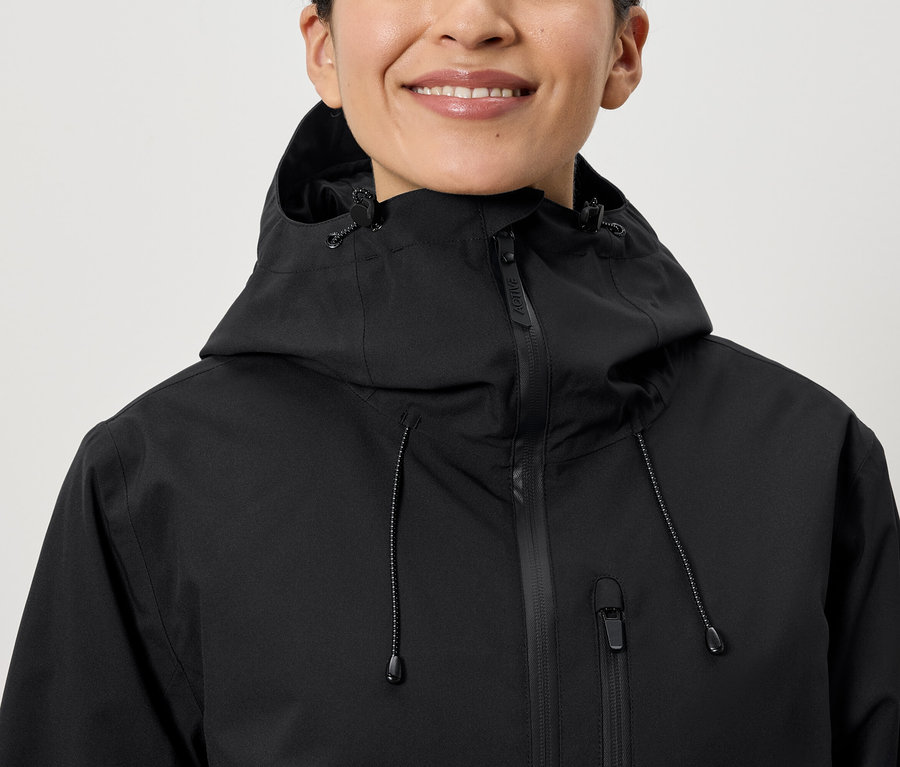 Egy mosolygó nő fekete kapucnis kabátot visel.