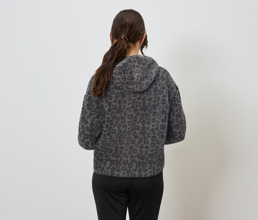 A háttal álló nő szürke, állatmintás kapucnis pulóvert és fekete nadrágot visel.