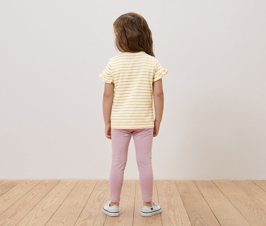 Hátulról látható lány sárga-fehér csíkos, fodros felsőben, rózsaszín leggingsben és fehér tornacipőben.