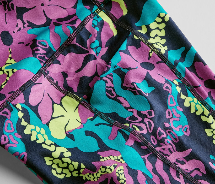 Közelkép egy 3/4-es sportnadrágról, melyen rózsaszín, türkiz és sárga virágok és levelek láthatók.