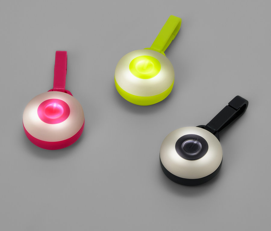 Három kerek lámpa csíptetővel rózsaszín, zöld és fekete színben, szürke háttéren.