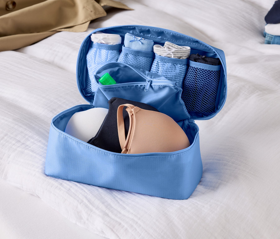 Nyitott, világoskék poggyászszervező melltartókkal és fehérneművel egy fehér lepedőn.