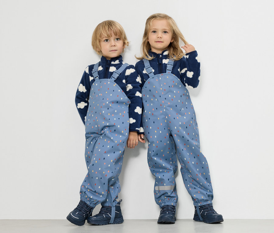 Két gyerek áll egymás mellett, egy fiú és egy lány, mindketten felhőmintás kék polár pulóvert és színes pöttyös kék esőnadrágot viselnek.