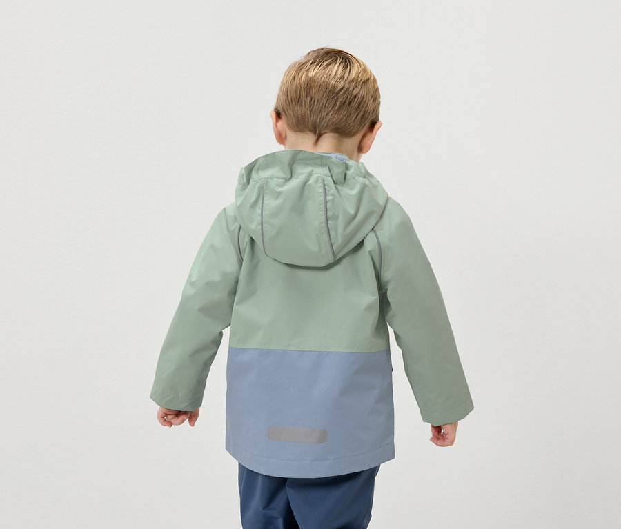 Hátulnézet egy szőke hajú gyerekről, aki kétszínű, zöld és kék kabátot visel.