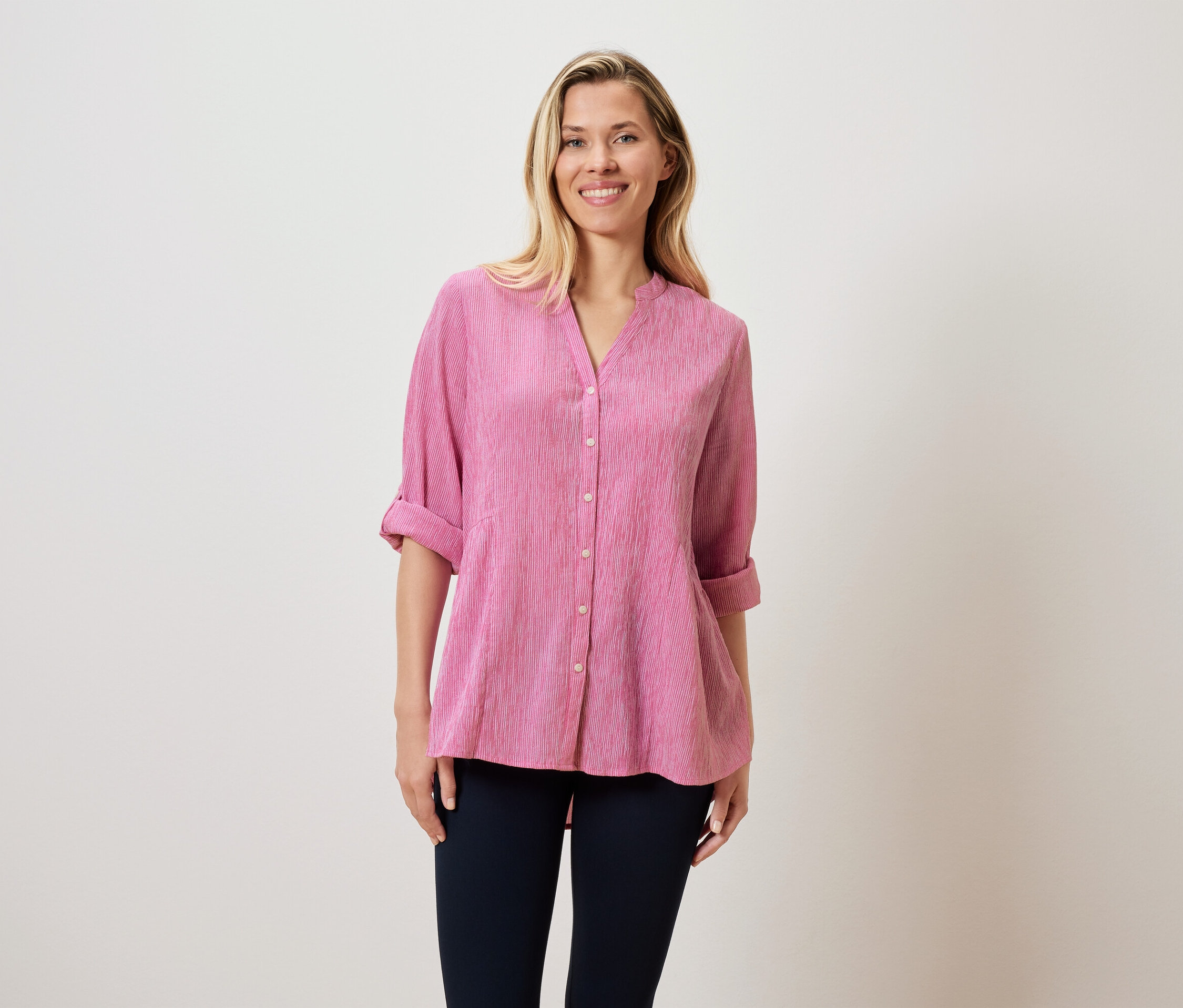 Egy szőke hajú nő rózsaszín blúzt és sötét nadrágot visel.