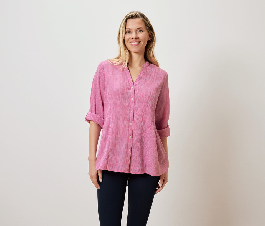 Egy szőke hajú nő rózsaszín blúzt és sötét nadrágot visel.