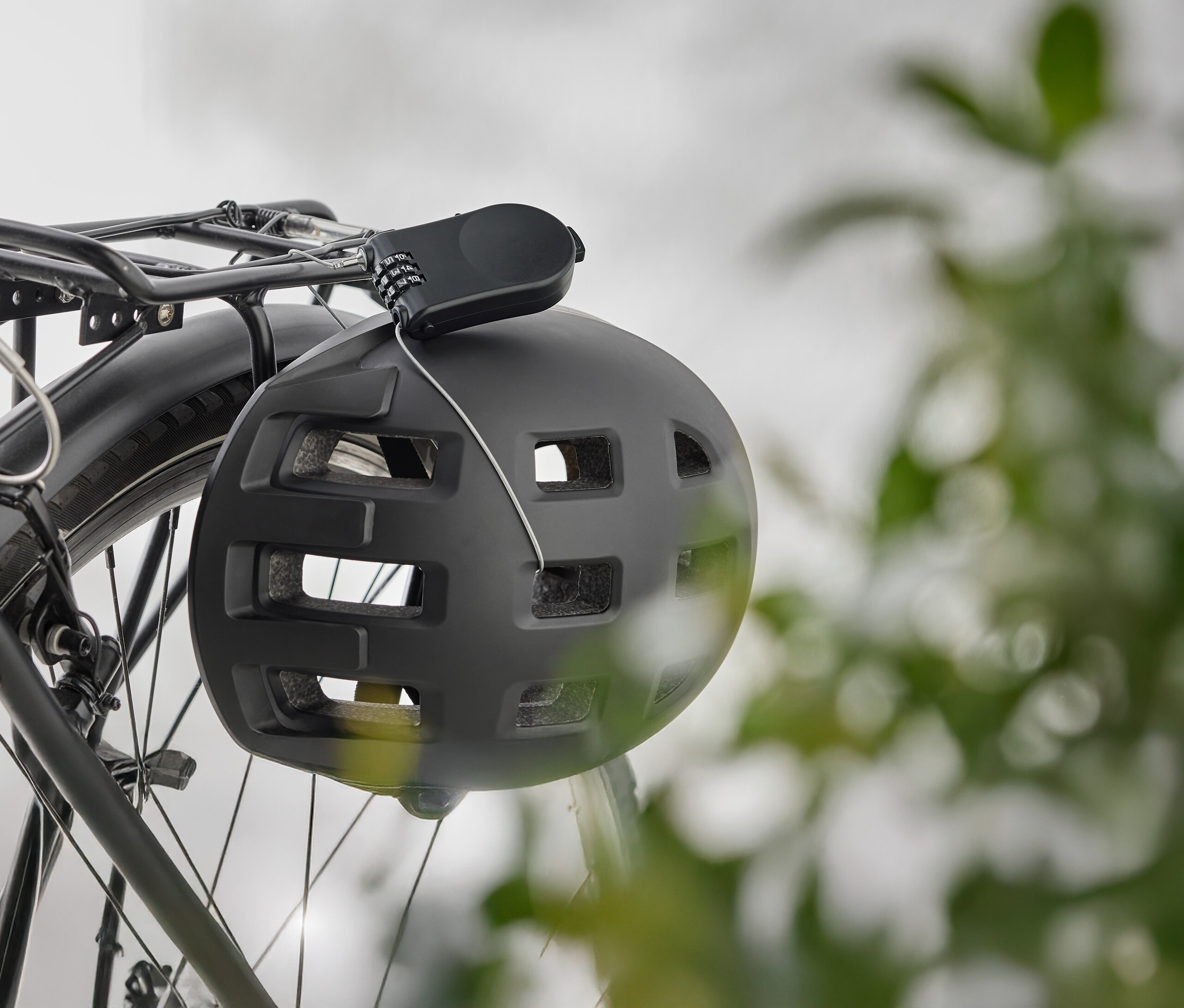 Egy fekete kerékpáros sisak lóg egy kerékpár csomagtartóján egy számzáras zárral.