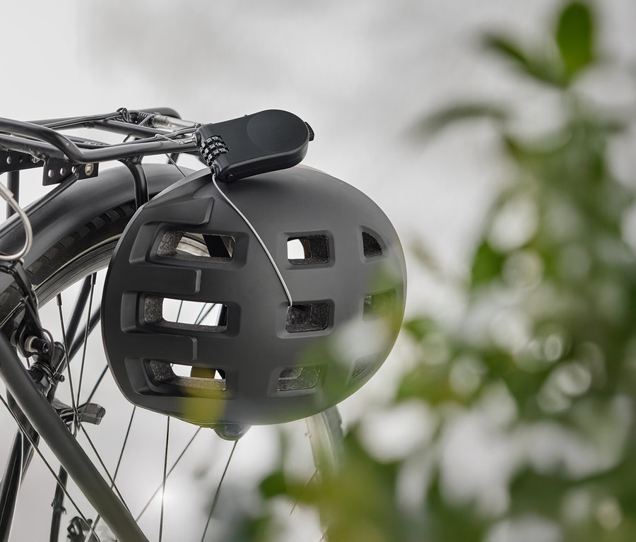 Egy fekete kerékpáros sisak lóg egy kerékpár csomagtartóján egy számzáras zárral.