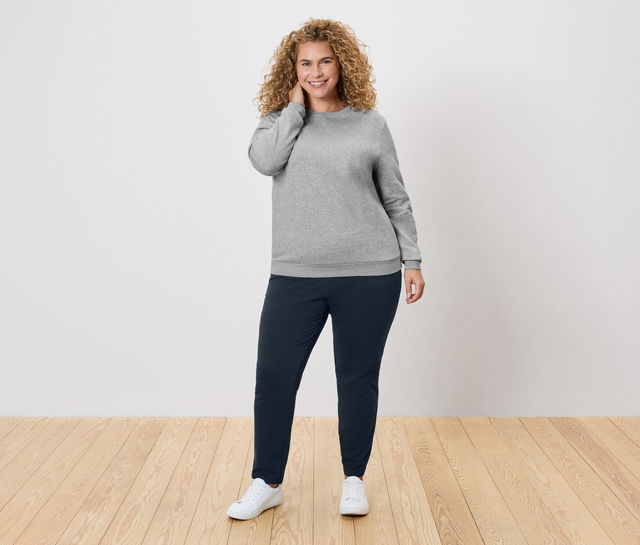 Göndör hajú nő szürke pulóverben és sötétkék nadrágban.