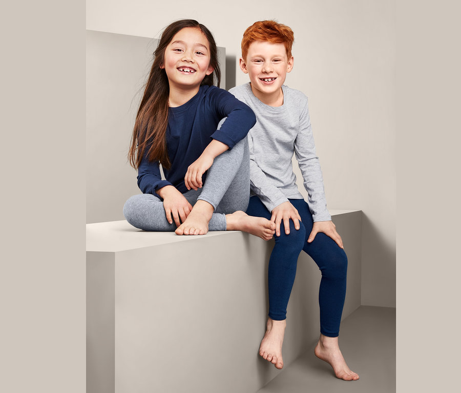 Két gyermek ül egy kockán, kék és szürke kötött leggings szettben.