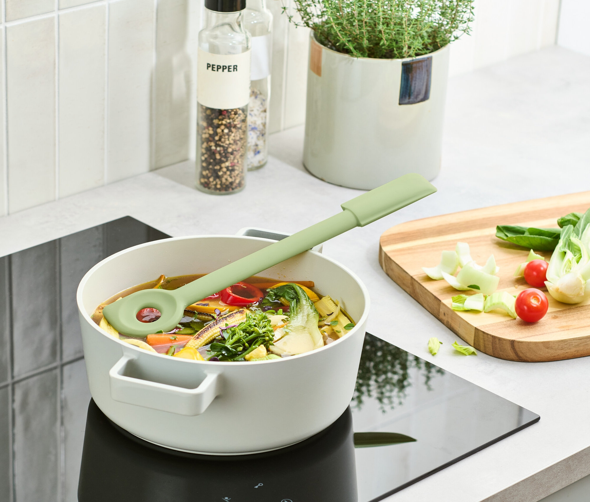 Egy zöld multifunkciós főzőkanál egy leveses fazékban fekszik egy indukciós főzőlapon.