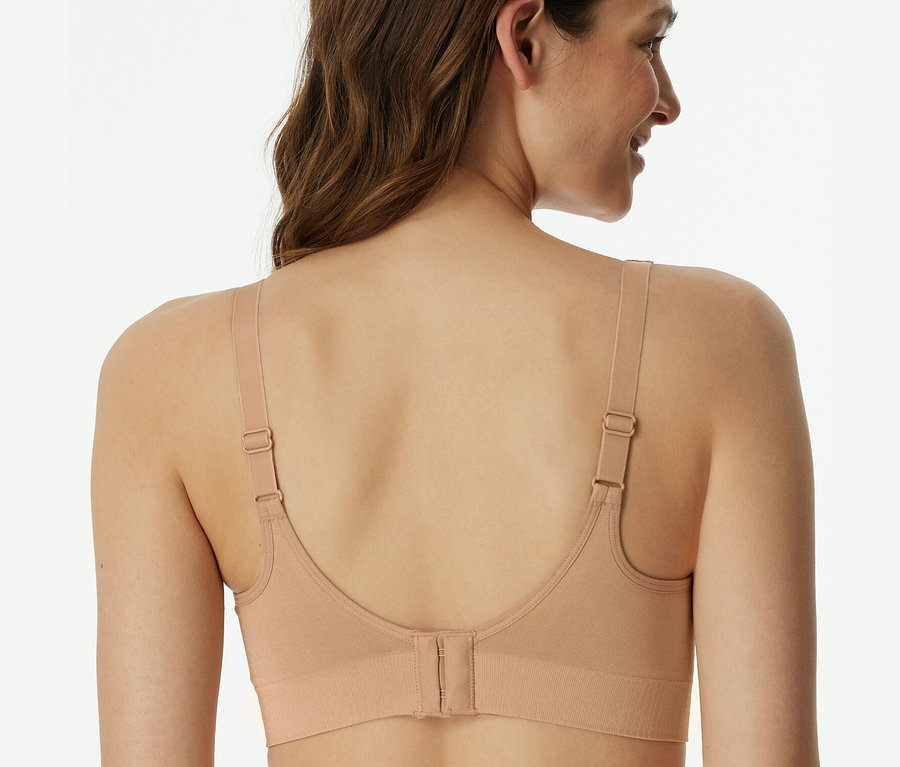 Hátulnézet egy barna hajú nőről, aki juharszínű, betétes, puha SCHIESSER melltartót visel.