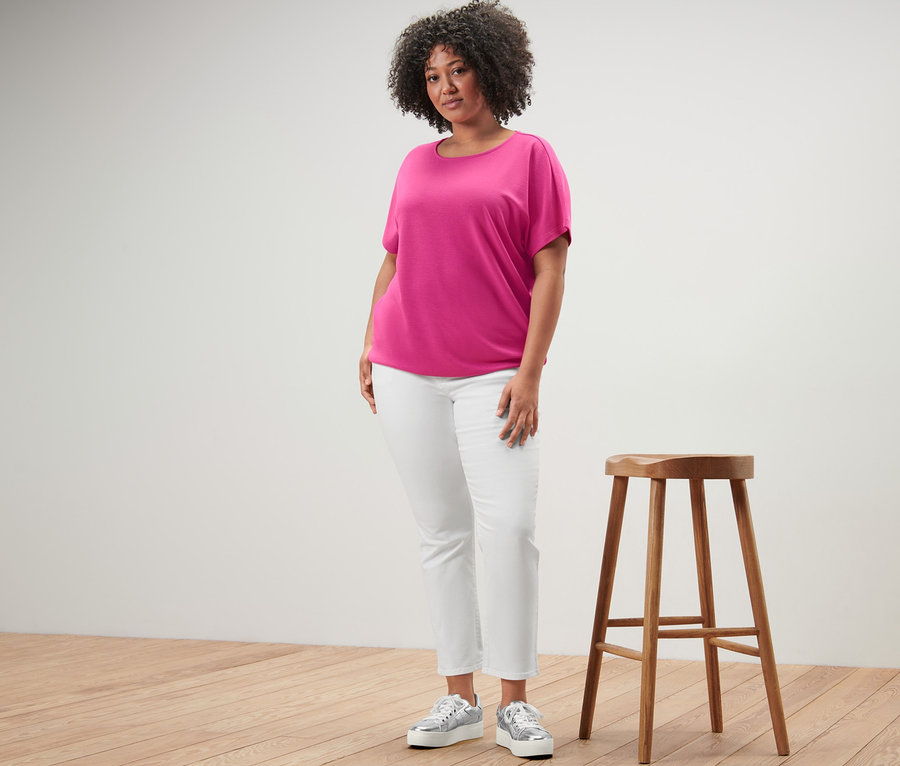 Nő áll egy fa szék mellett, női pólóblúzt és Színes farmernadrágot – Fit »Emma«, krém színben visel.