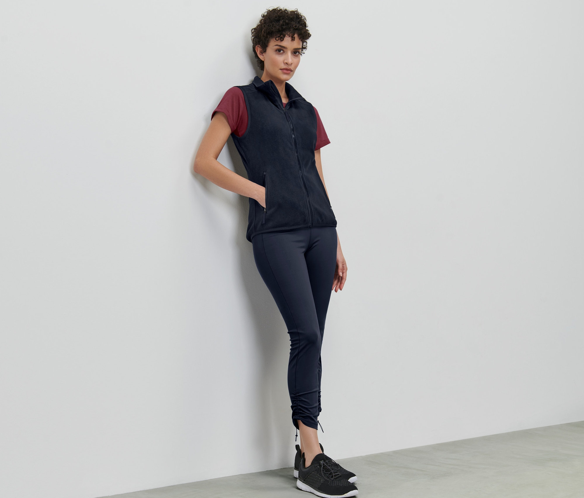 Egy nő a falnak dőlve sötétkék polármellényt visel.