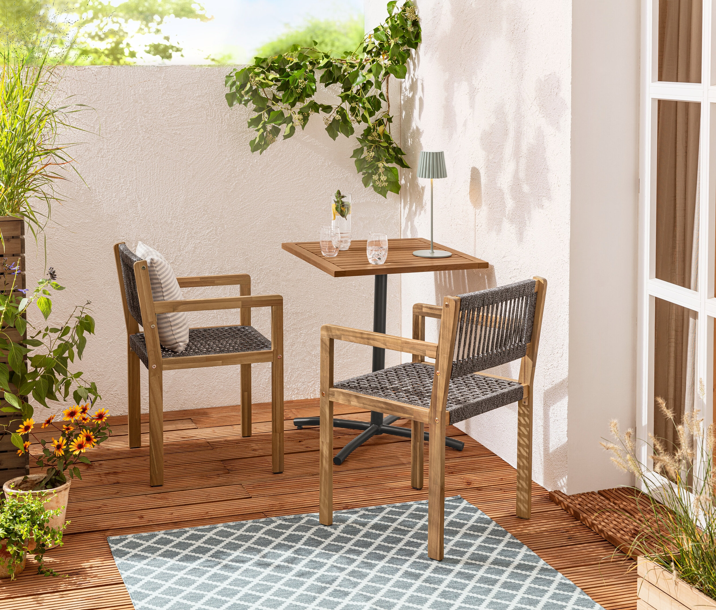 Két textilhálós ebédlőszék áll egy »Elin« erkélyre való asztal mellett egy kültéri megfordítható szőnyegen.