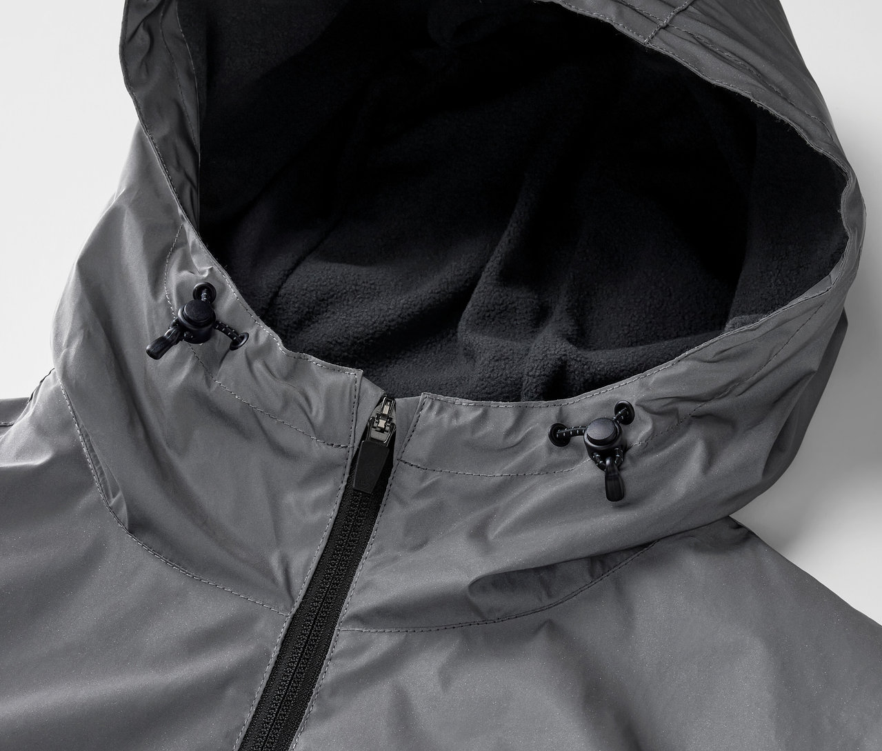 Egy szürke, fényvisszaverő sportkabát részlete cipzárral és kapucnival.