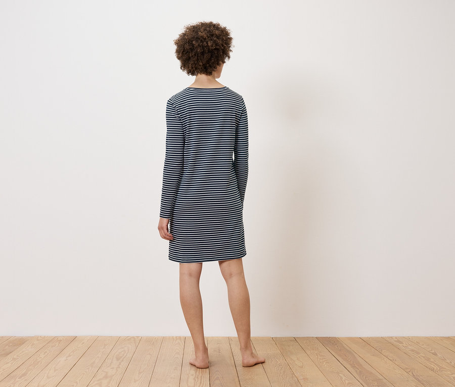 Egy nő áll háttal a kamerának, csíkos ruhát visel.