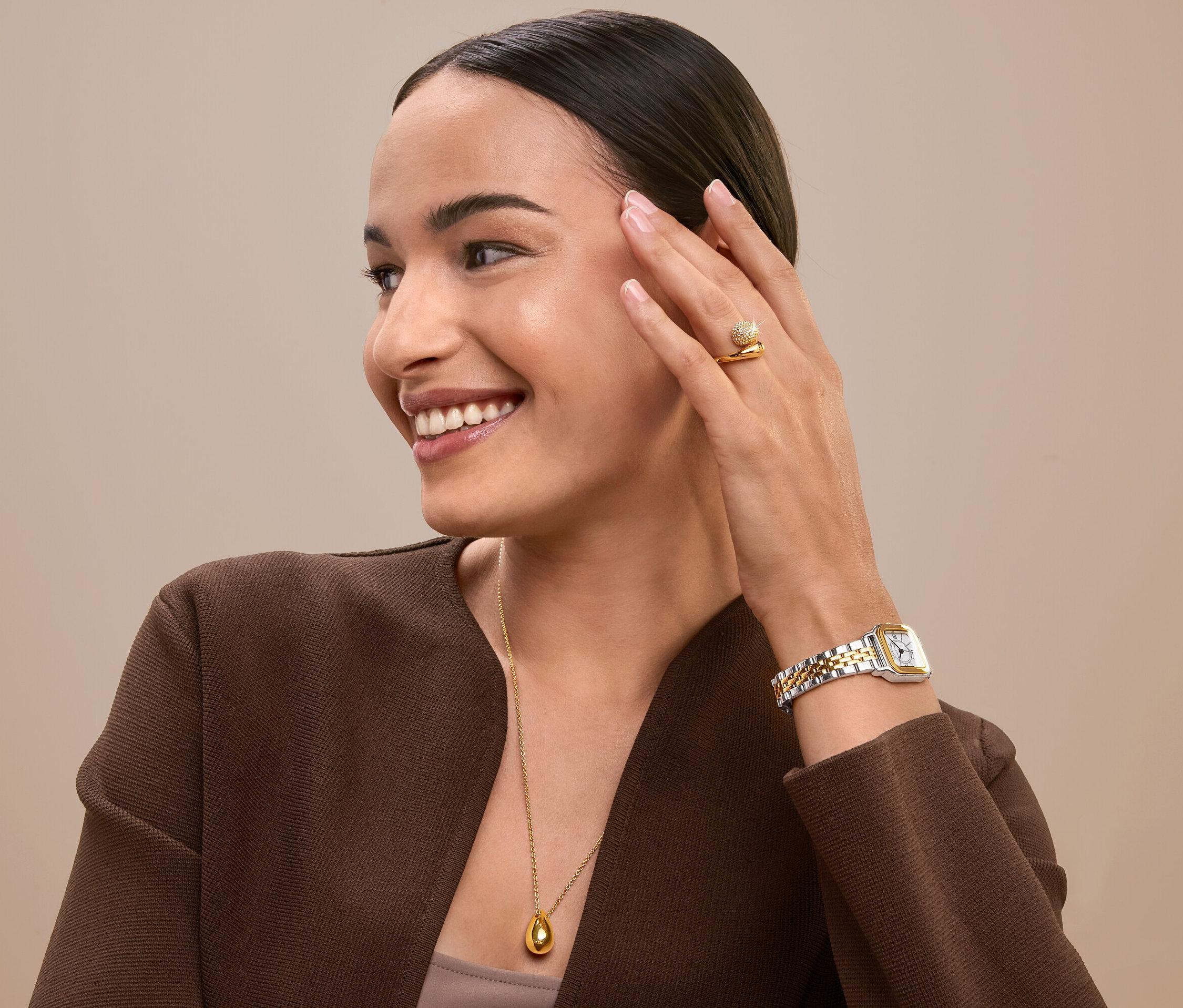 Mosolygó nő arca érintésével, arany gyűrűt, órát és nyakláncot visel.
