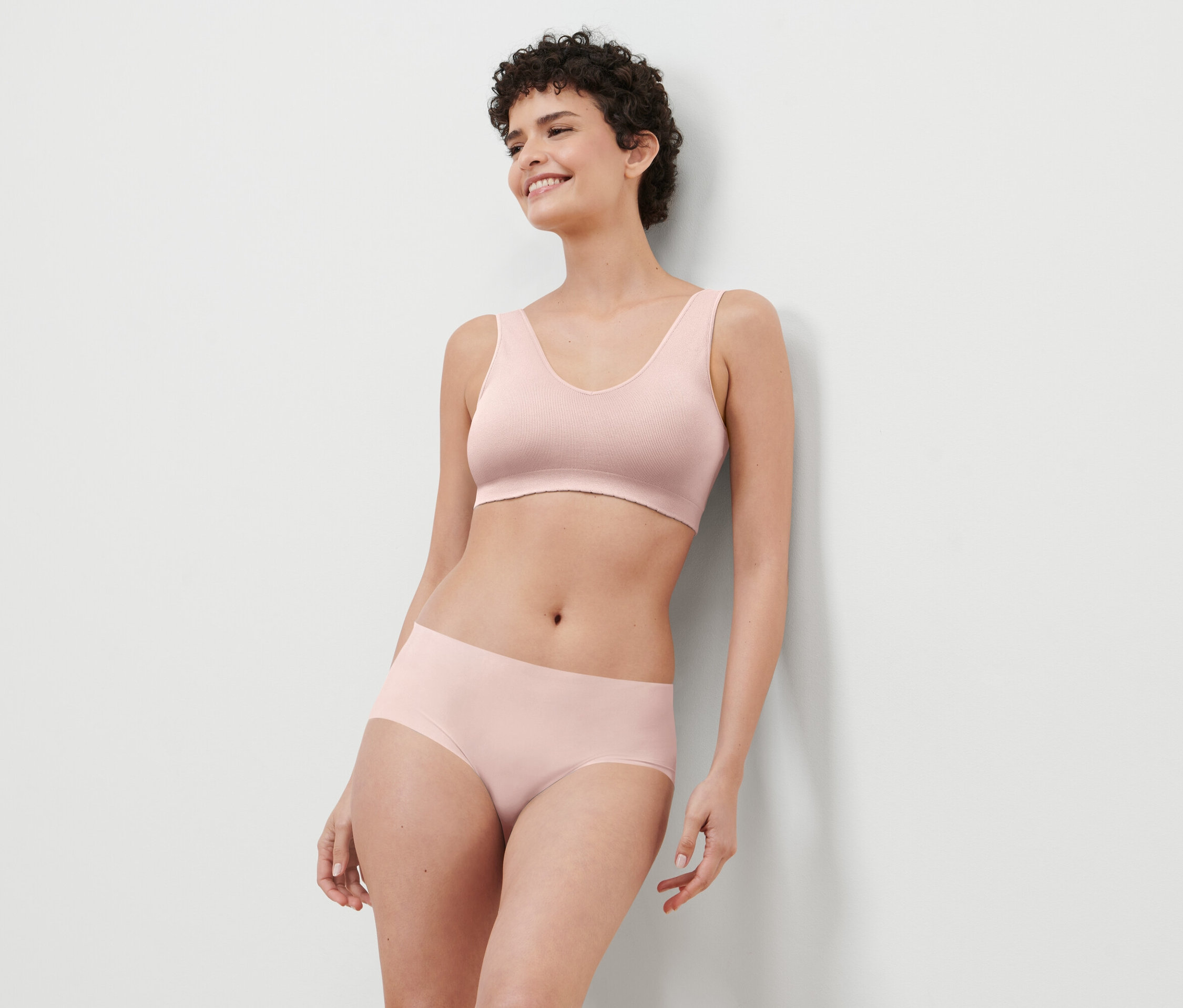 Rövid hajú nő rózsaszín melltartót és bugyit visel.