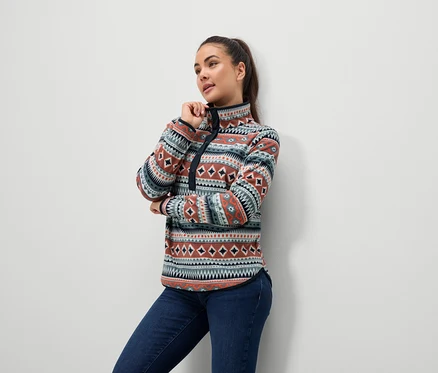 Nő mintás fleece pulóvert és farmert visel.